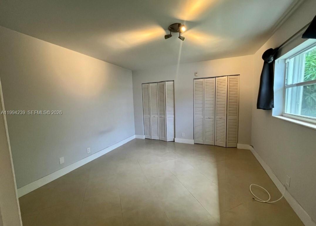 An empty bedroom features light gray walls, tile flooring, two louvered closets, and a window — 1824 Monroe St # 14, Hollywood FL 33020, HOLLYWOOD, FL