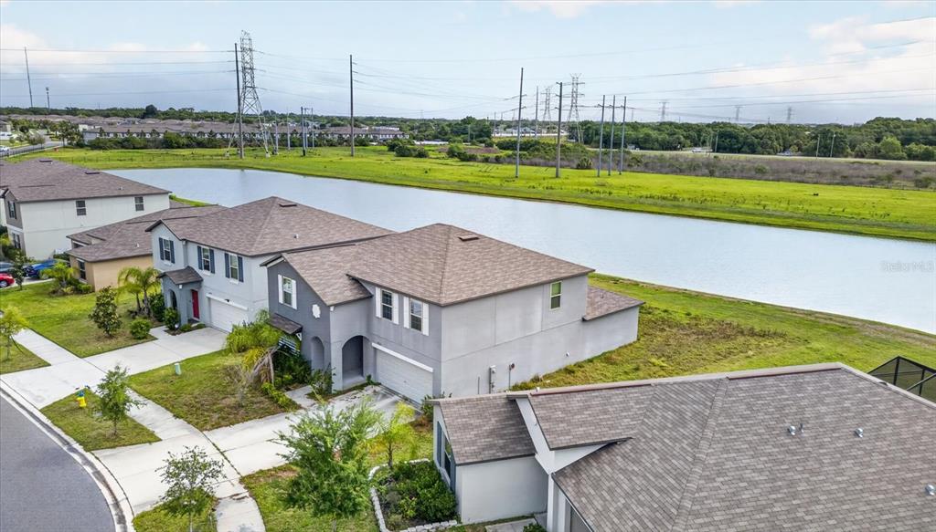 An aerial view shows suburban houses with gray stucco siding situated beside a long pond — 4712 WILD SENNA BOULEVARD, TAMPA, FL