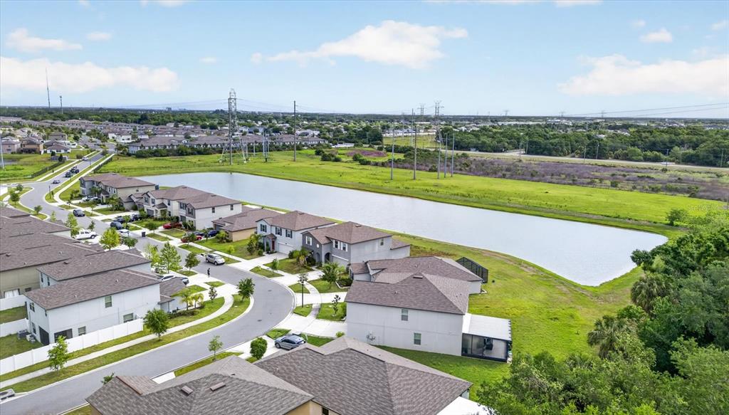An aerial view shows suburban houses near a large retention pond and power lines — 4712 WILD SENNA BOULEVARD, TAMPA, FL