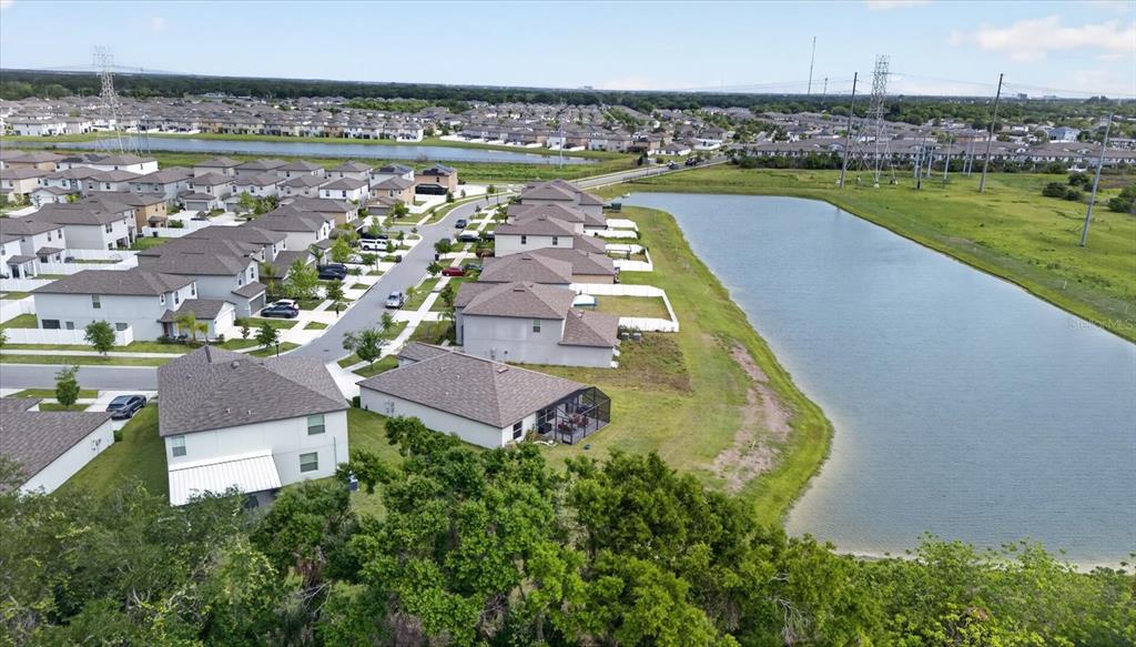 An aerial view shows a suburban neighborhood with houses bordering a large retention pond — 4712 WILD SENNA BOULEVARD, TAMPA, FL