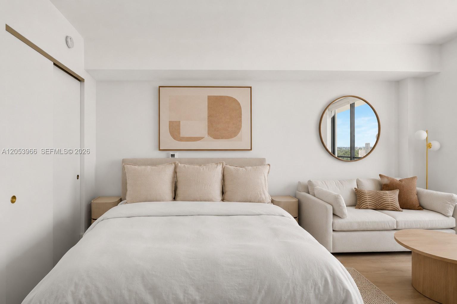 A bedroom features a bed with beige pillows, a sofa, and a round wall mirror — 90 NE 32nd St # 825, Miami FL 33127, MIAMI, FL