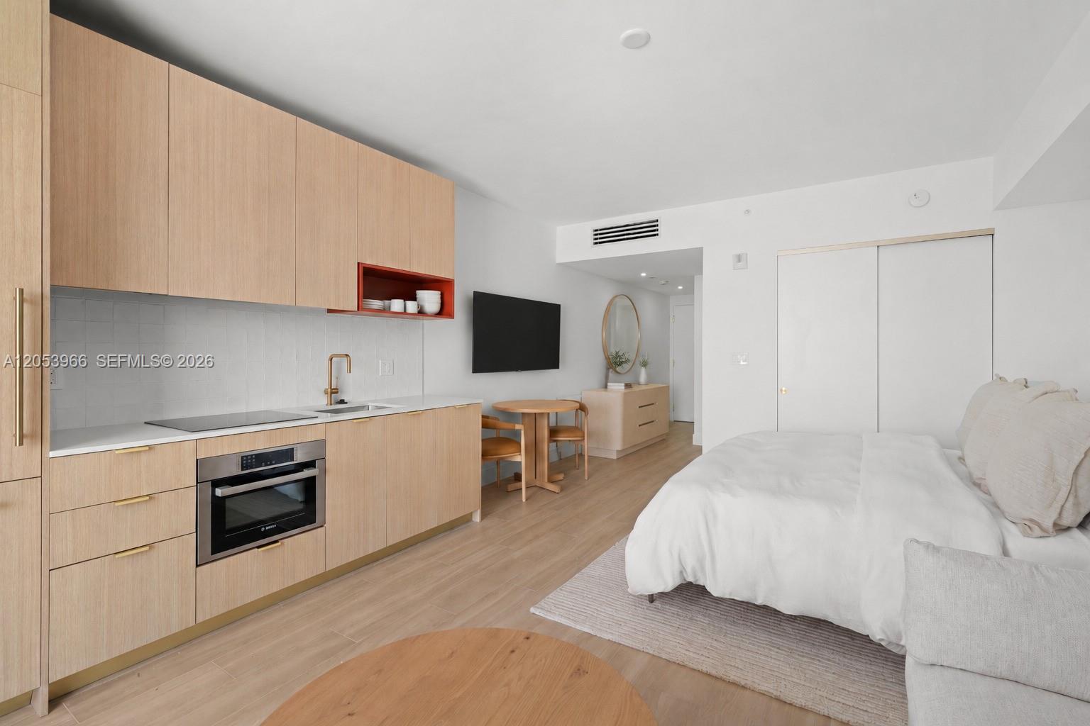 A studio apartment features a kitchenette with light wood cabinets, a dining table, and bed — 90 NE 32nd St # 825, Miami FL 33127, MIAMI, FL