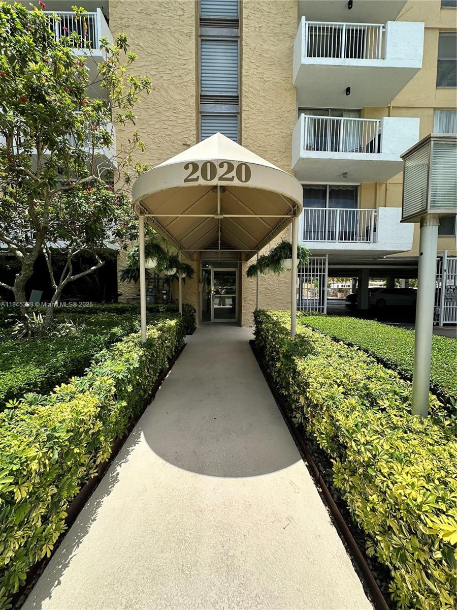 A concrete walkway leads to the entrance of a multi-story building under a beige awning — 2020 NE 135th St # 807, North Miami FL 33181, NORTH MIAMI, FL