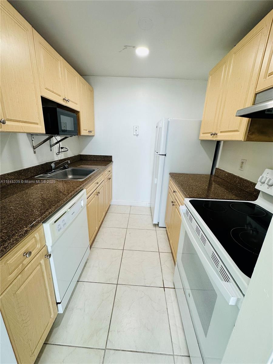 A galley kitchen features light wood cabinets, dark granite countertops, and white appliances — 2020 NE 135th St # 807, North Miami FL 33181, NORTH MIAMI, FL