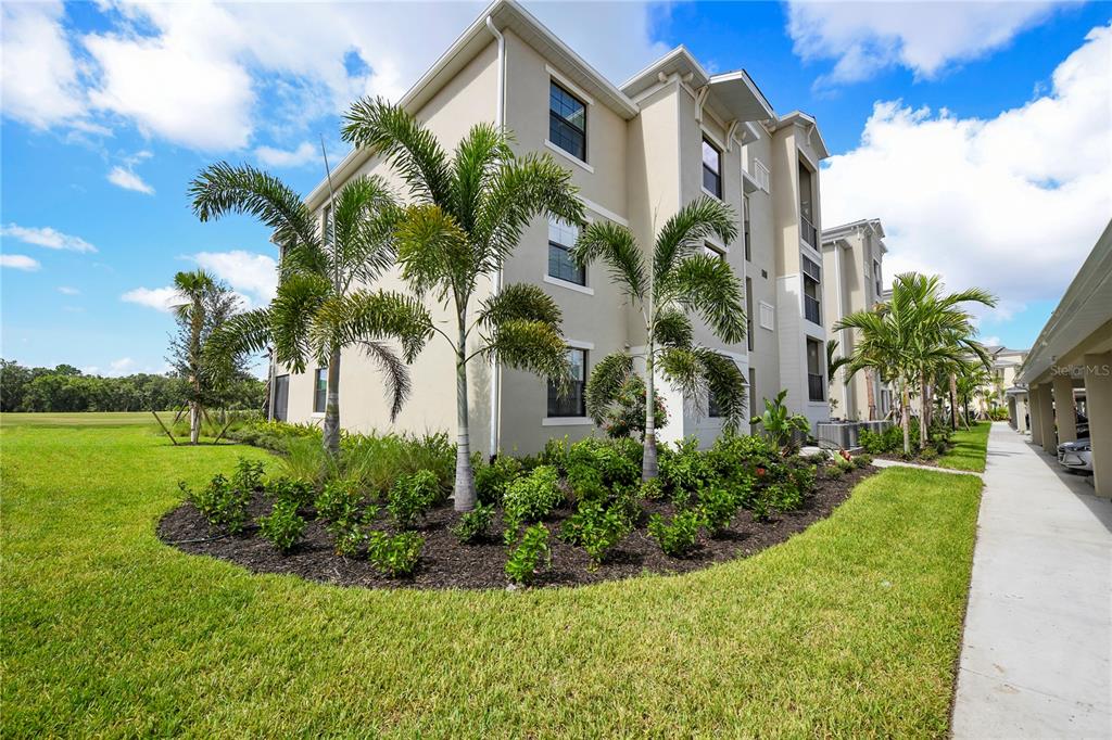 A multi-story apartment building exterior features palm trees and landscaping next to a paved walkway — 17810 GAWTHROP STREET UNIT 101, LAKEWOOD RANCH, FL