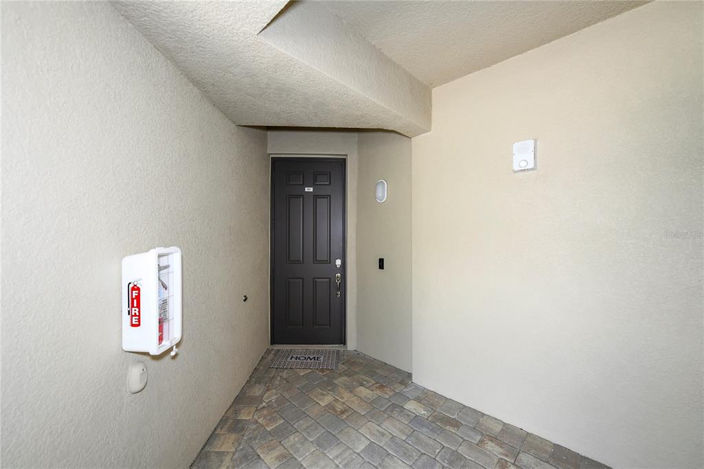A dark gray front door is set in a recessed entryway with stone-look tile flooring — 17810 GAWTHROP STREET UNIT 101, LAKEWOOD RANCH, FL