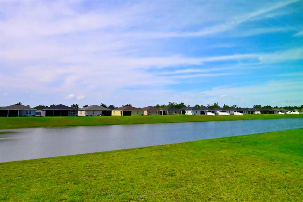 A wide view of a residential pond bordered by green grass and suburban houses — 3540 74TH AVENUE CIRCLE E, SARASOTA, FL