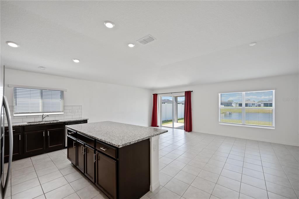 A kitchen with dark cabinets and a granite island opens into a bright living area — 3540 74TH AVENUE CIRCLE E, SARASOTA, FL