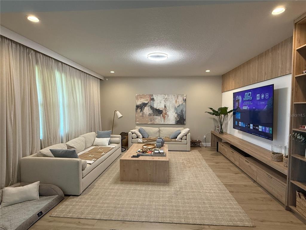 A modern living room features two beige sofas, a wooden coffee table, and a wall-mounted television — 14428 CRESTAVISTA AVENUE, CLERMONT, FL