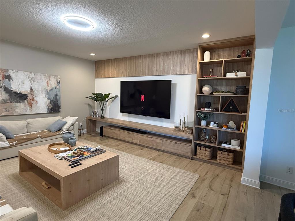 A living room features a large wall-mounted television, custom wood cabinetry, and a matching coffee table — 14428 CRESTAVISTA AVENUE, CLERMONT, FL