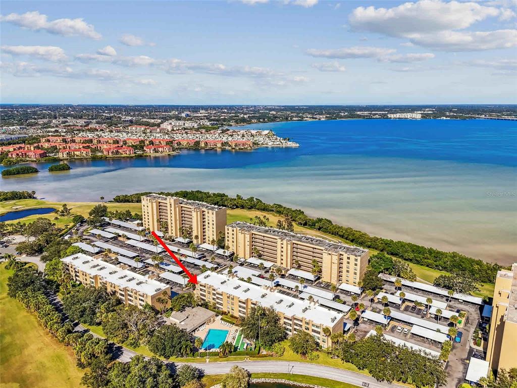 An aerial view shows several multi-story apartment buildings surrounded by green space and water — 2615 COVE CAY DRIVE UNIT 409, CLEARWATER, FL