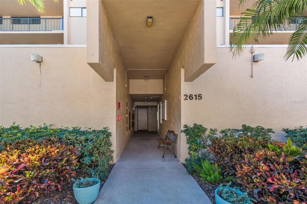 An exterior view of a covered building entrance with a walkway and a wooden bench — 2615 COVE CAY DRIVE UNIT 409, CLEARWATER, FL