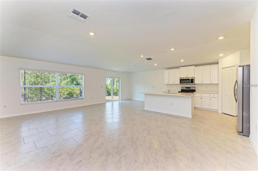 An open-concept kitchen and living area with white cabinets, tile flooring, and sliding glass doors — 1207 SHEEHAN BOULEVARD, PORT CHARLOTTE, FL