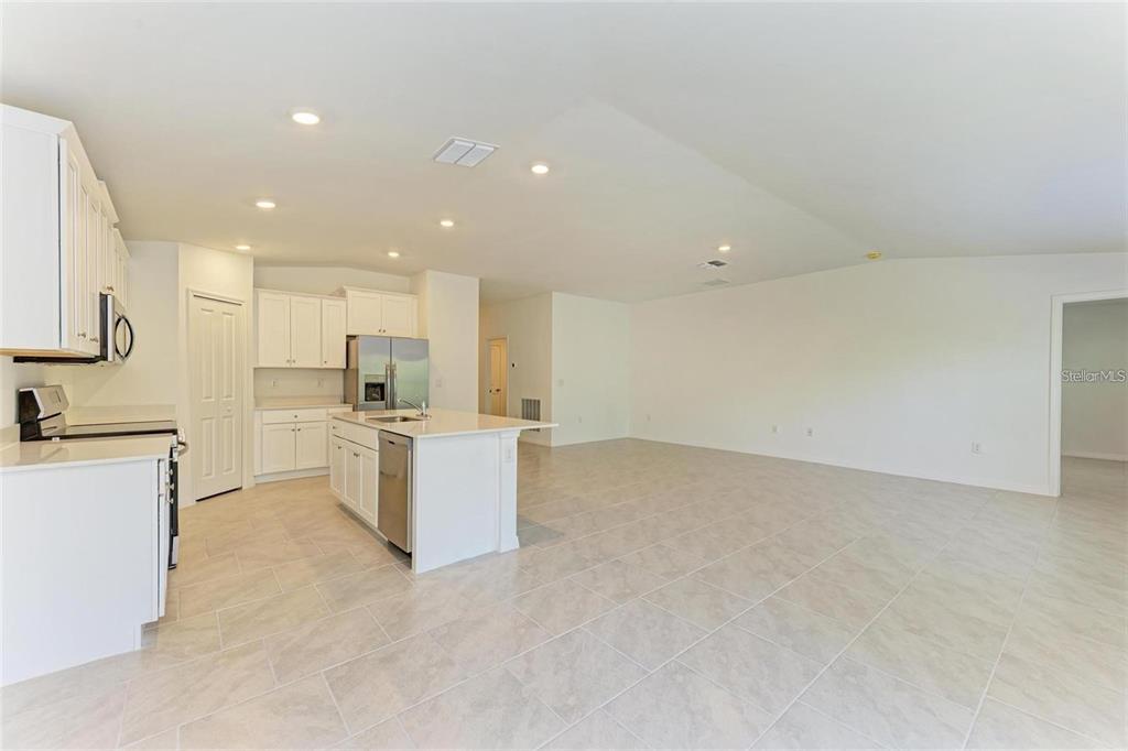 A kitchen with white cabinets, a center island, and tile flooring opens to a living area — 1207 SHEEHAN BOULEVARD, PORT CHARLOTTE, FL