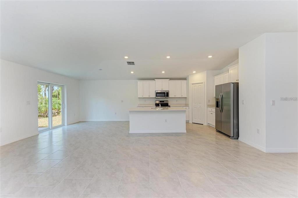 A bright, open-concept kitchen and living area features white cabinetry, stainless appliances, and tile flooring — 1207 SHEEHAN BOULEVARD, PORT CHARLOTTE, FL