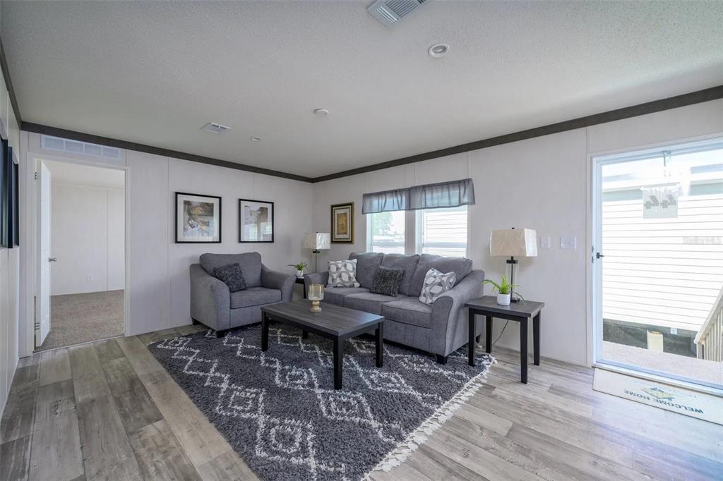 A living room features gray furniture, a patterned rug, and wood-look flooring — 1041 NE COUNTY ROAD 125, LAWTEY, FL