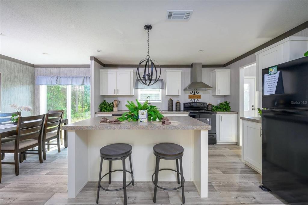 A kitchen features a central island with two stools, white cabinetry, and stainless steel appliances — 1041 NE COUNTY ROAD 125, LAWTEY, FL