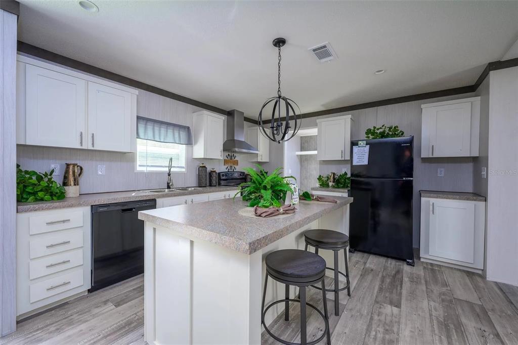 A kitchen features white cabinets, a central island with bar stools, and black appliances — 1041 NE COUNTY ROAD 125, LAWTEY, FL