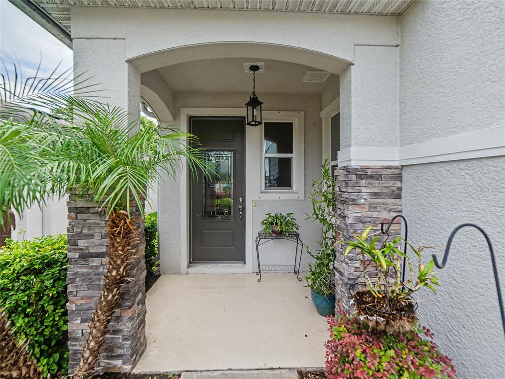 A covered front entryway features a dark gray door, stone pillars, and potted plants — 7508 SUNSHINE BRIDGE AVENUE, GIBSONTON, FL