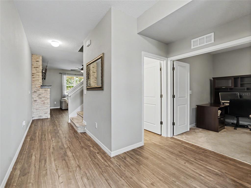 A hallway with wood-look flooring leads to a stone fireplace, stairs, and a home office — 7508 SUNSHINE BRIDGE AVENUE, GIBSONTON, FL
