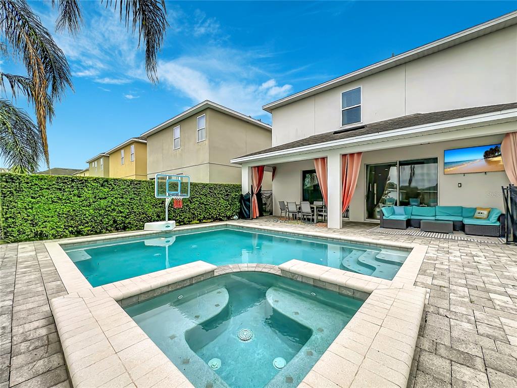 A backyard features a swimming pool, a raised spa, and a covered patio with furniture — 7546 MARKER AVENUE, KISSIMMEE, FL