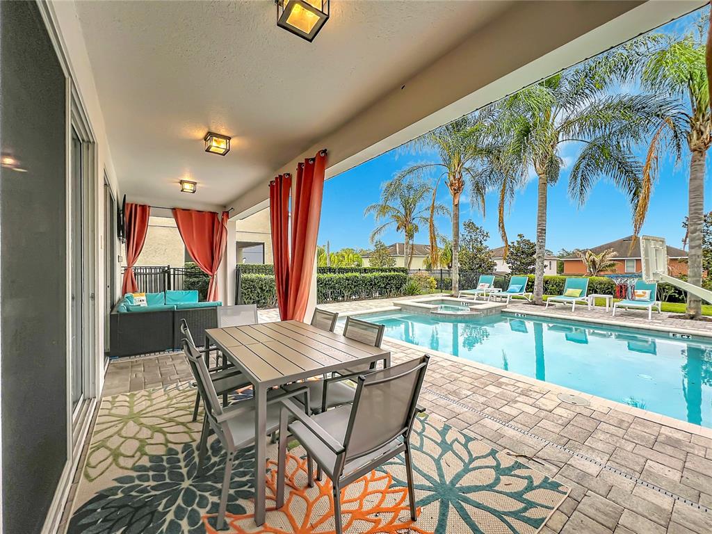 A covered patio with a dining set overlooks a swimming pool and palm trees — 7546 MARKER AVENUE, KISSIMMEE, FL