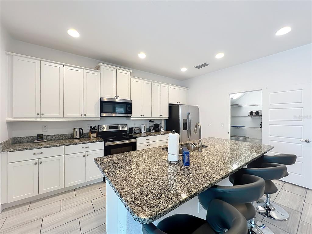 A kitchen features white cabinets, granite countertops, a center island, and stainless steel appliances — 7546 MARKER AVENUE, KISSIMMEE, FL