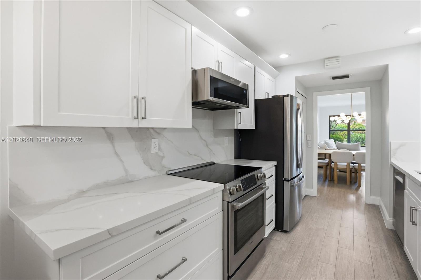 A modern kitchen features white cabinets, marble-style countertops, stainless steel appliances, and light wood flooring — 830 Greensward Ct # H, Delray Beach FL 33445, DELRAY BEACH, FL
