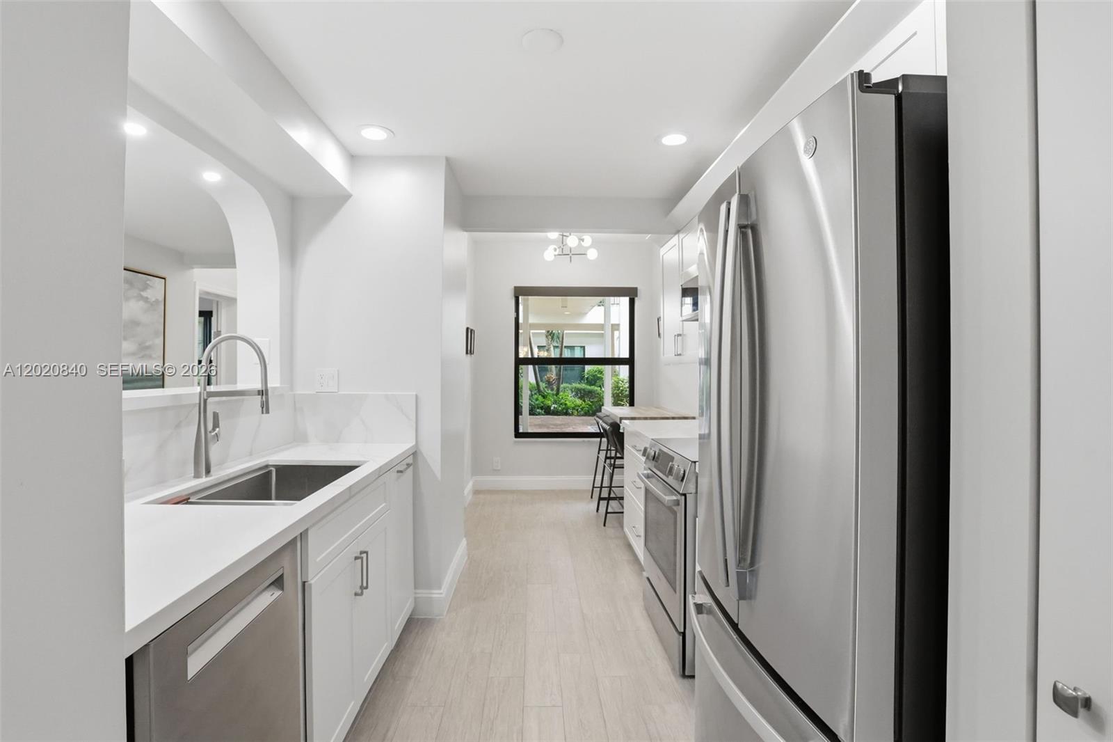 A modern galley kitchen features white cabinetry, stainless steel appliances, and light wood-look flooring — 830 Greensward Ct # H, Delray Beach FL 33445, DELRAY BEACH, FL
