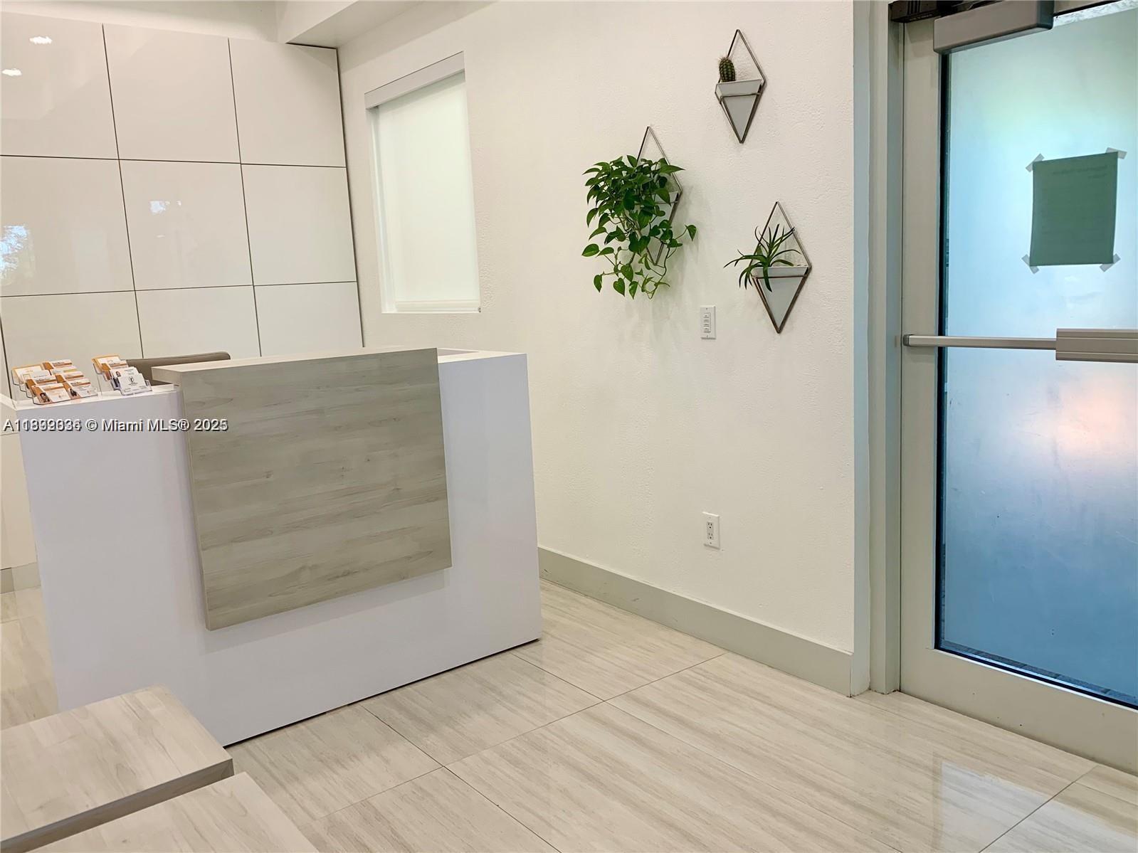 A modern reception area features a white desk, wood-look paneling, wall-mounted planters, and tiled flooring — 17100 Royal Palm Blvd # 1, Weston FL 33326, WESTON, FL