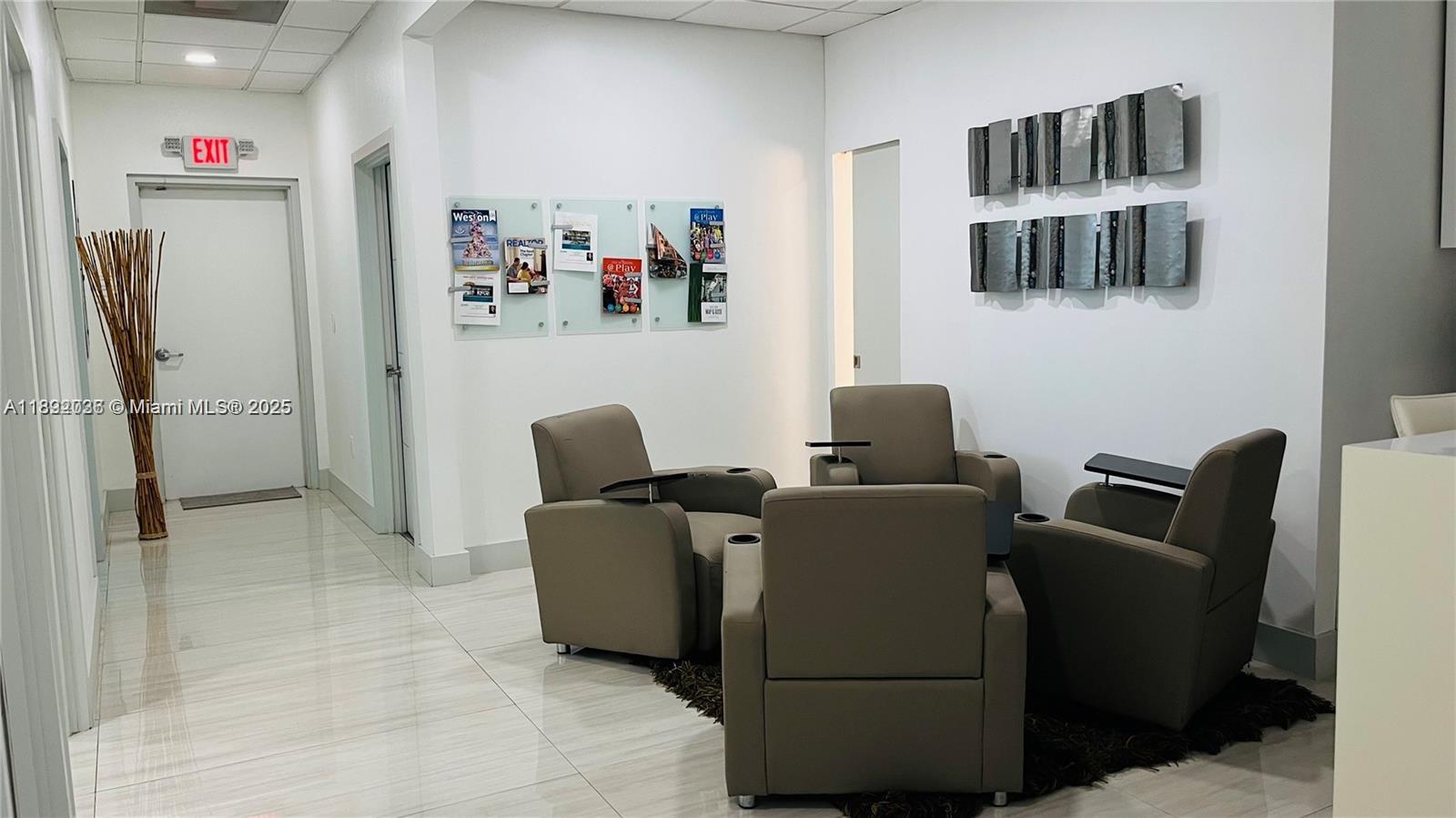 A waiting area features four gray armchairs on a rug with wall-mounted magazine displays — 17100 Royal Palm Blvd # 1, Weston FL 33326, WESTON, FL