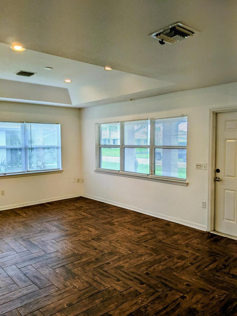 An empty room features herringbone-patterned wood floors, white walls, and windows with horizontal blinds — 1804 Blue Heron Lane # C, Fort Pierce FL 34982, FORT PIERCE, FL