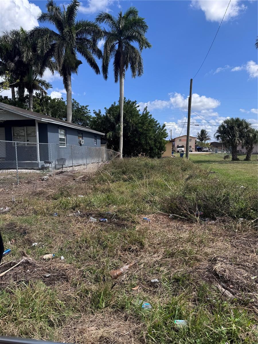 A grassy, unkempt lot sits next to a gray house with a chain-link fence — 609 SW 8th St, Belle Glade FL 33430, BELLE GLADE, FL