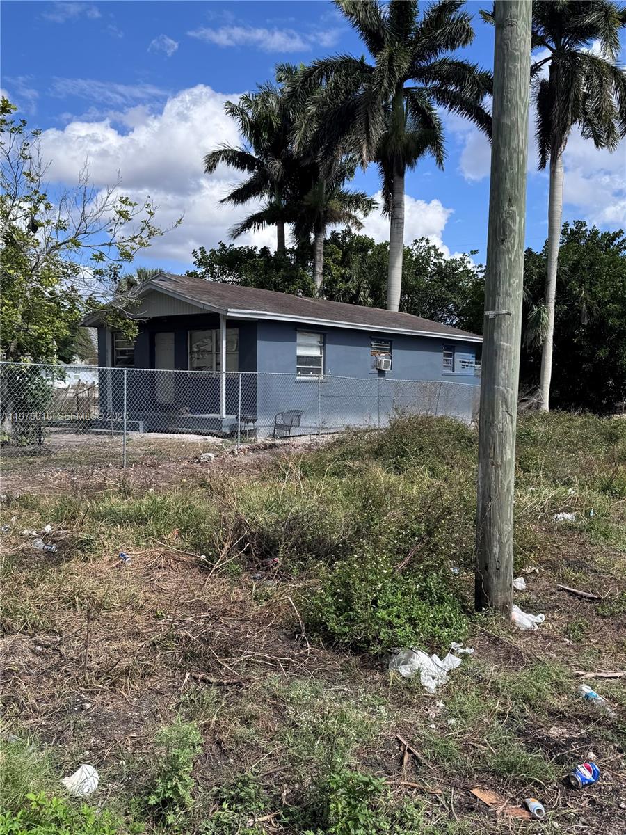 A blue single-story house sits behind a chain-link fence on a grassy, unkempt lot — 609 SW 8th St, Belle Glade FL 33430, BELLE GLADE, FL