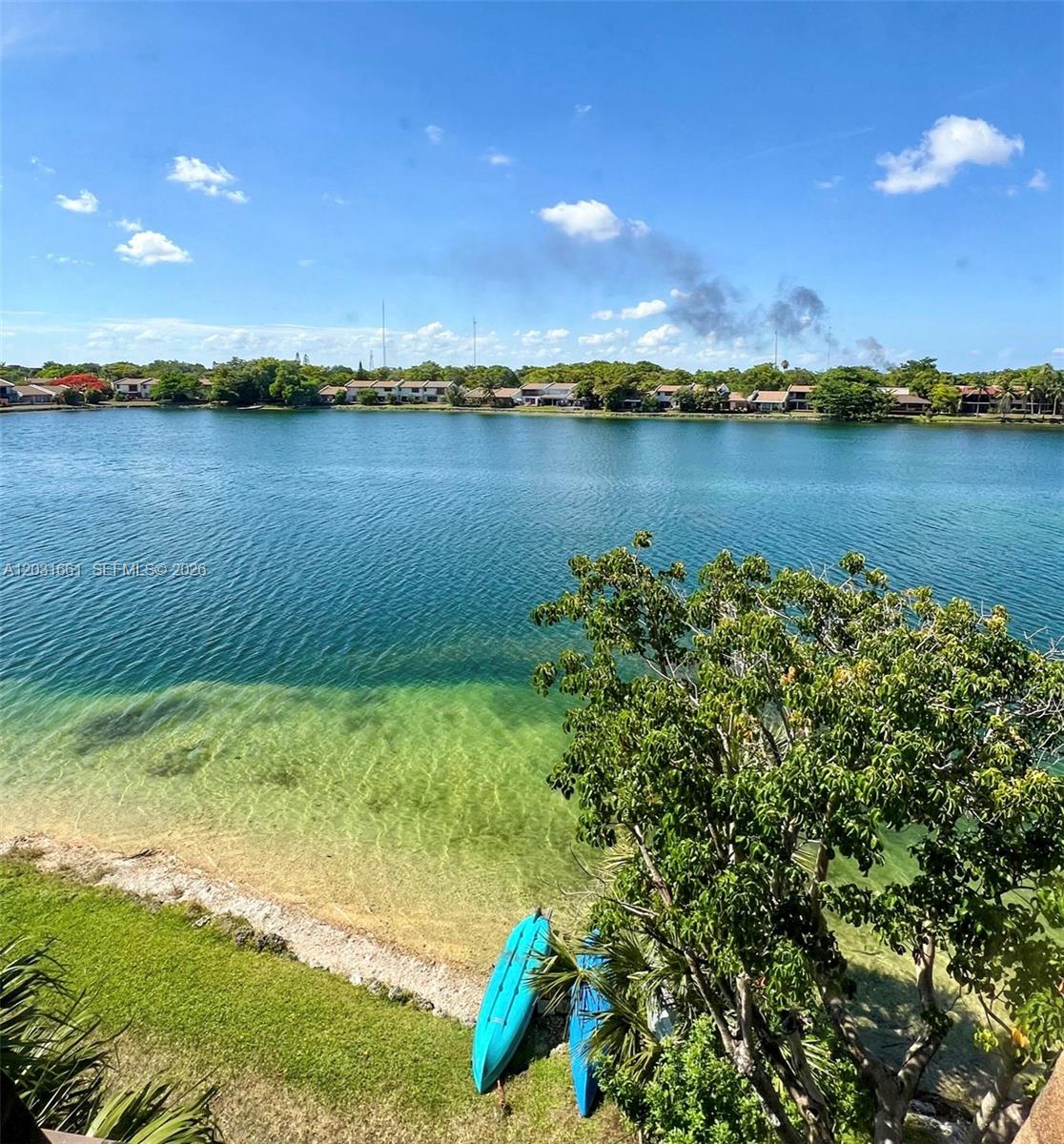 A view of a lake with two kayaks on the shore and houses in the background — 671 NE 195th St, Miami FL 33179, MIAMI, FL