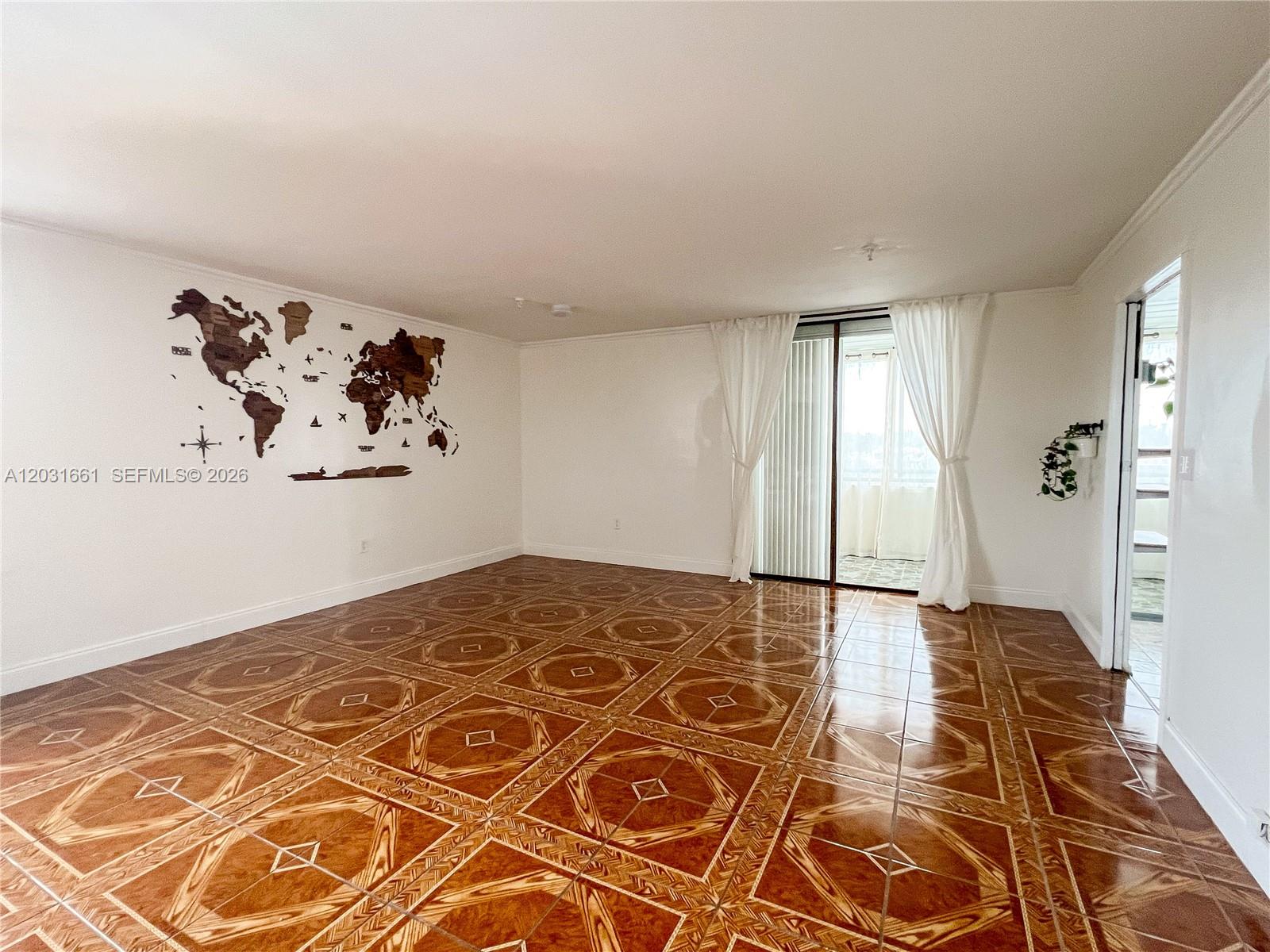 An empty room features patterned brown tile flooring, a world map wall decoration, and balcony access — 671 NE 195th St, Miami FL 33179, MIAMI, FL