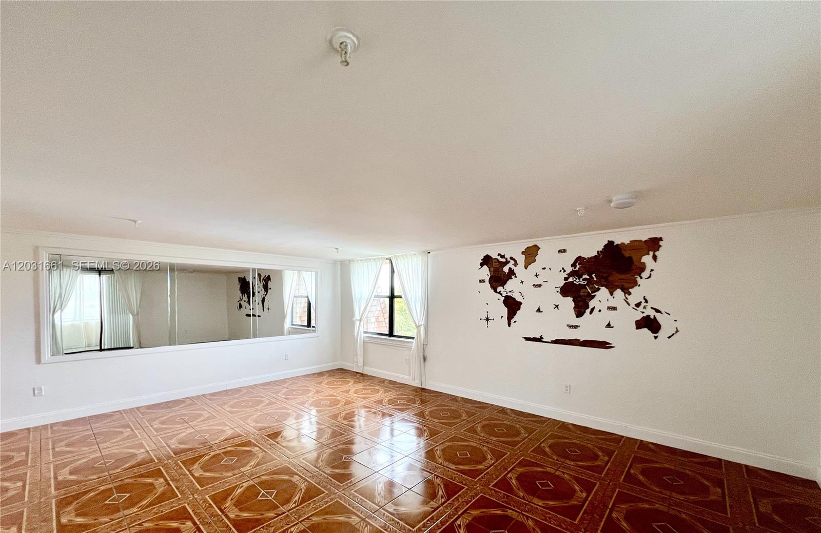 An empty room features tiled flooring, a large wall mirror, and a wooden world map decoration — 671 NE 195th St, Miami FL 33179, MIAMI, FL