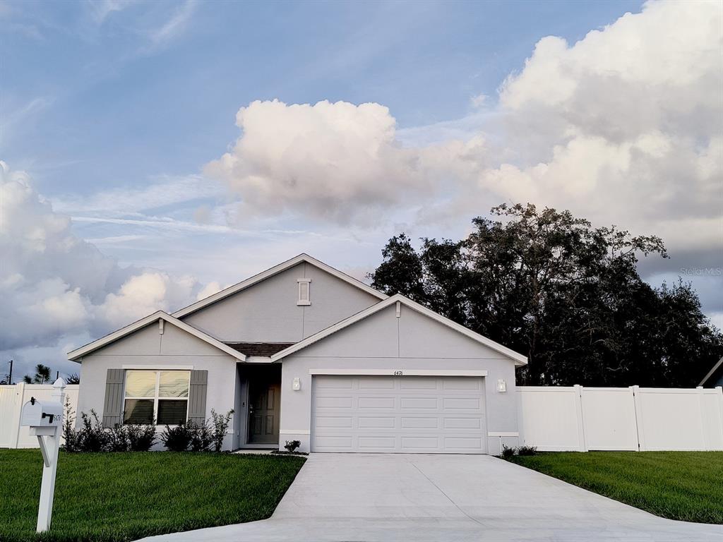 A single-story house with a light gray exterior, a two-car garage, and a white fence — 6476 MELACANO AVENUE, SPRING HILL, FL