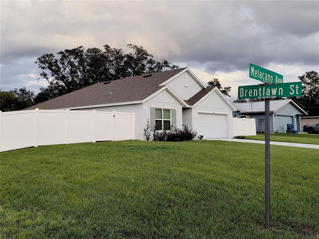 A single-story house with a white vinyl fence and a street sign in the foreground — 6476 MELACANO AVENUE, SPRING HILL, FL
