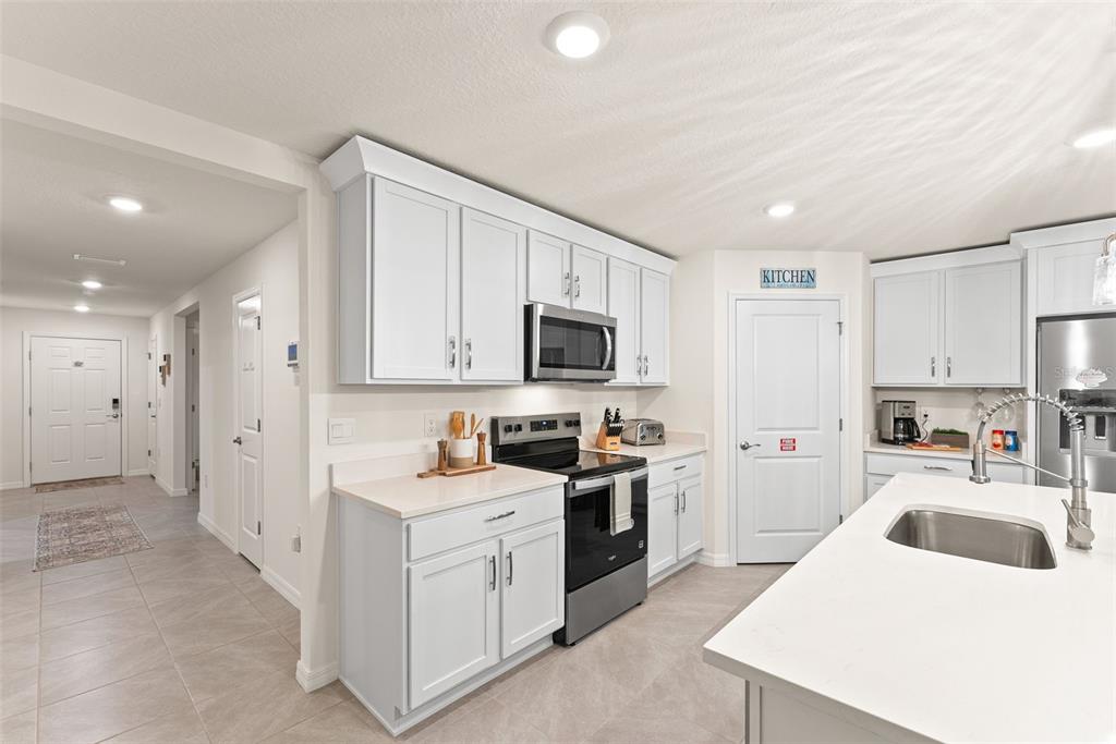 A modern kitchen features white cabinets, stainless steel appliances, and a central island with sink — 6476 MELACANO AVENUE, SPRING HILL, FL