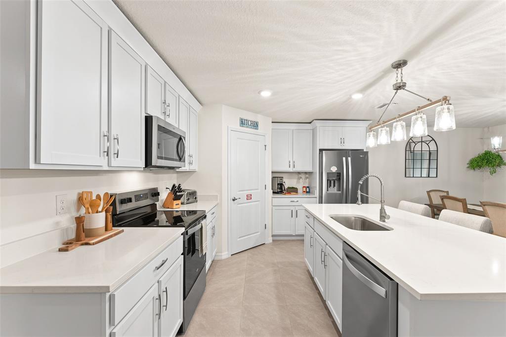 A modern kitchen features white cabinetry, quartz countertops, a center island, and stainless steel appliances — 6476 MELACANO AVENUE, SPRING HILL, FL