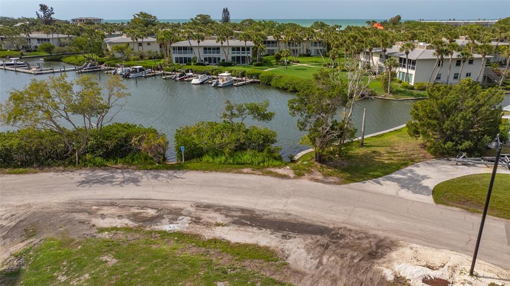 An aerial view shows a canal with docked boats, surrounding residential buildings, and a paved road — 6800 LONGBOAT DRIVE S, LONGBOAT KEY, FL