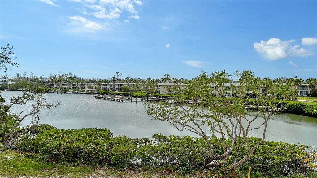 A view of a calm waterway lined with docks, lush vegetation, and multi-story residential buildings — 6800 LONGBOAT DRIVE S, LONGBOAT KEY, FL