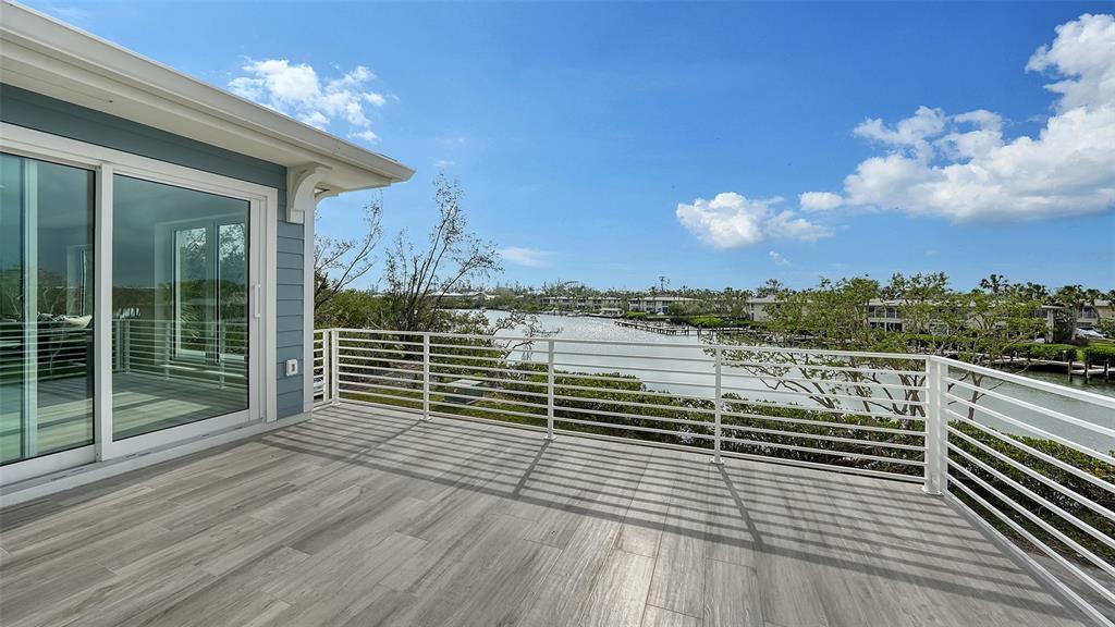 A balcony with wood-look tile flooring and a white railing overlooks a waterfront canal view — 6800 LONGBOAT DRIVE S, LONGBOAT KEY, FL