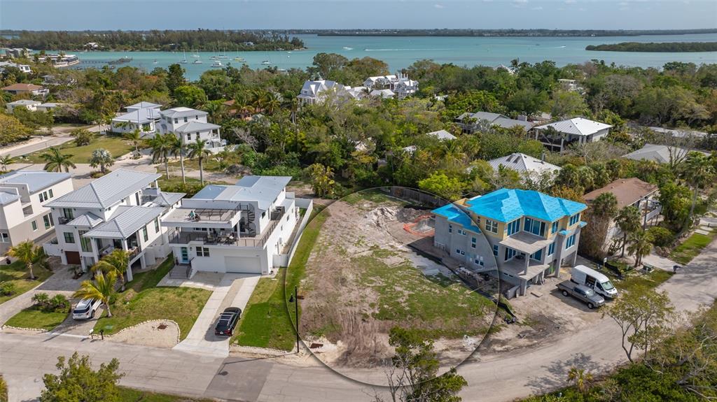An aerial view shows a vacant residential lot situated between two multi-story houses near water — 6800 LONGBOAT DRIVE S, LONGBOAT KEY, FL