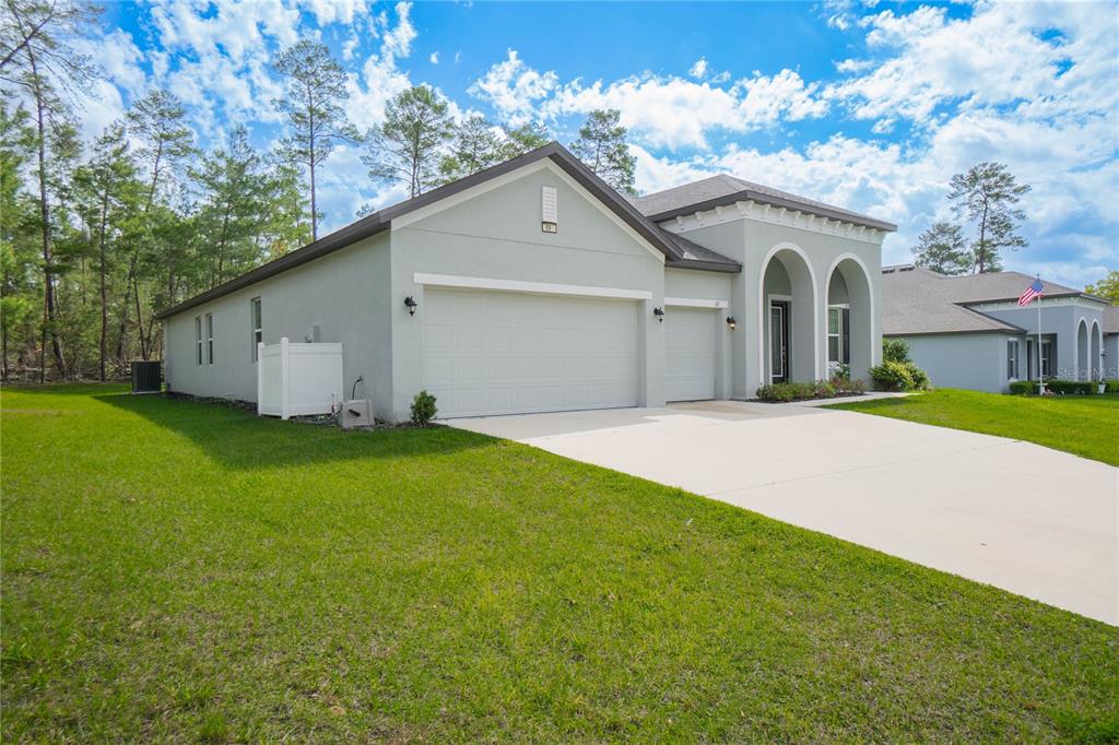 A light-colored single-story house with a three-car garage and arched entryway sits on a lawn — 69 GRASS STREET, HOMOSASSA, FL