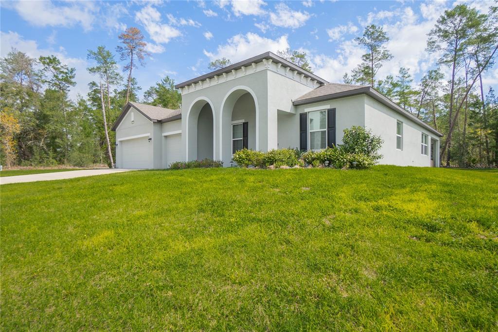 A light-colored single-story house with a two-car garage and arched entryway sits on a lawn — 69 GRASS STREET, HOMOSASSA, FL