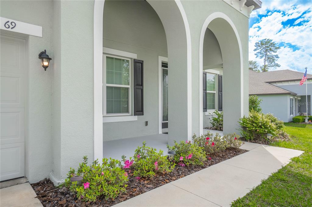 A light-colored house exterior features a covered front porch with arched entryways and landscaping — 69 GRASS STREET, HOMOSASSA, FL