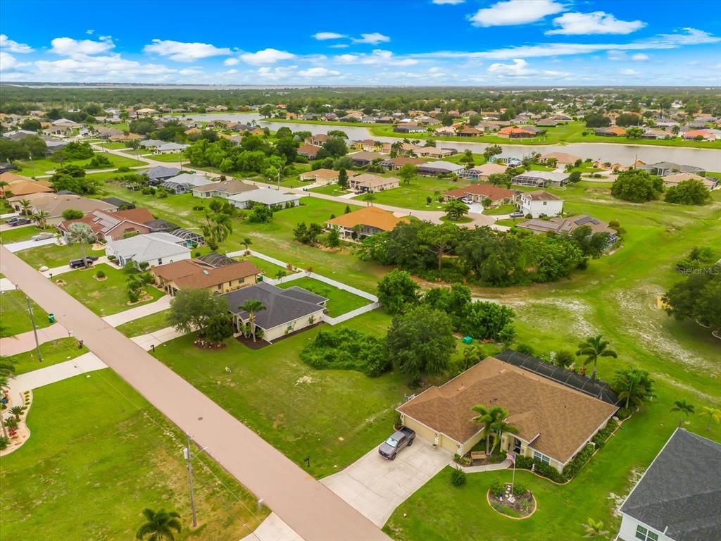 An aerial view shows a suburban neighborhood with single-family homes, green lawns, and a lake — 2381 MAURITANIA ROAD, PUNTA GORDA, FL