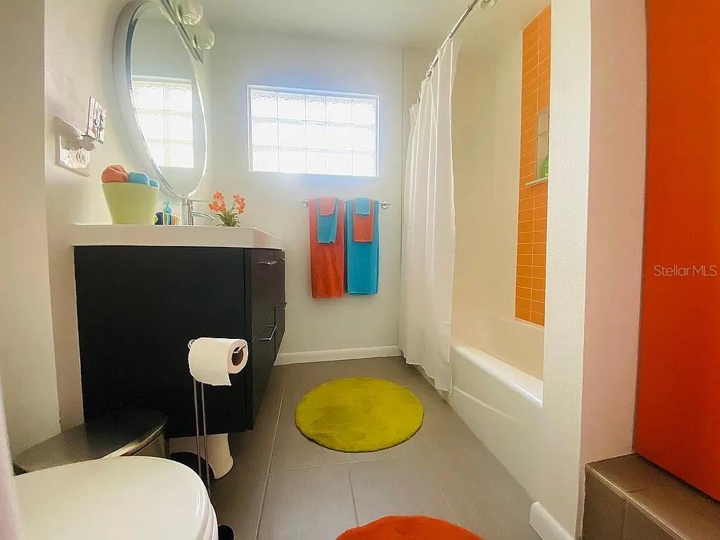 A bright orange front door sits next to glass block windows and a paved patio — 1402 CUMBIE STREET, ORLANDO, FL